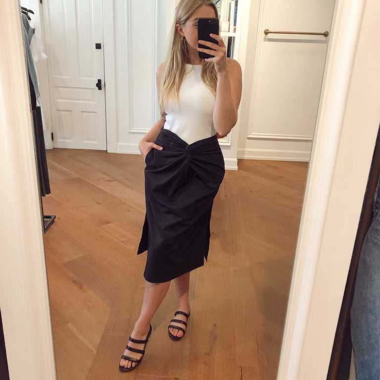 Social media selfie shot of the maria midi skirt with knot detailing in black, paired with black slide sandals and a white bodysuit.