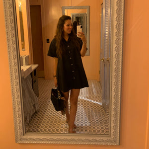 A social media selfie featuring the Amy button up collared dress in black. Styled with a black bag and nude strappy heels.