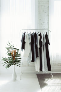 An editorial shot of the capsule collection hanging on a white rack with a plant next to it.